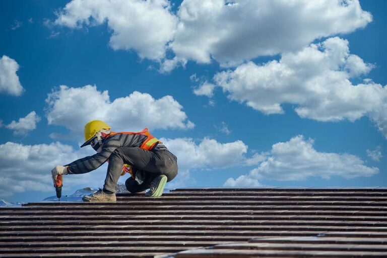 A person removing debris from a house roof with hand tools under cloudy skies.